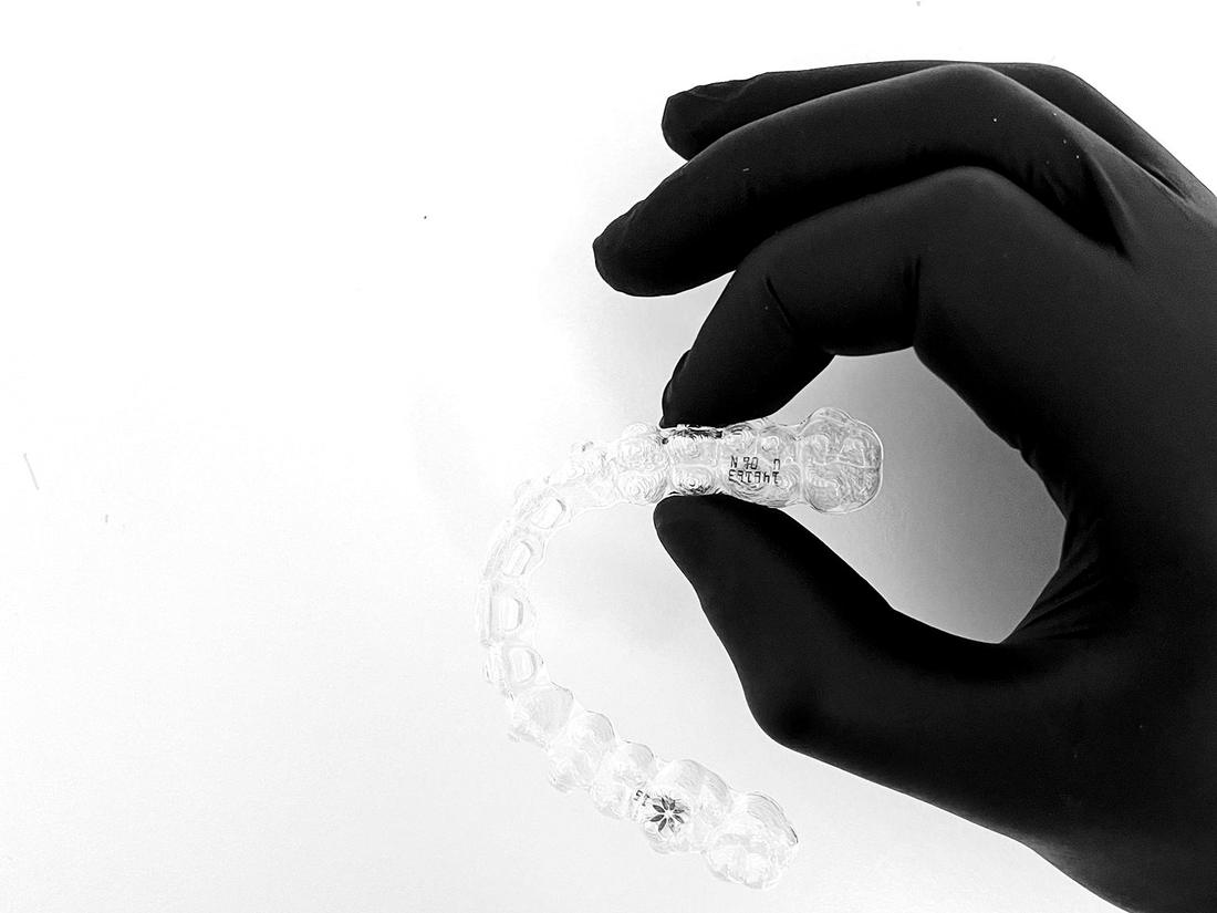 Una mano guantata di nero tiene una mascherina trasparente Invisalign