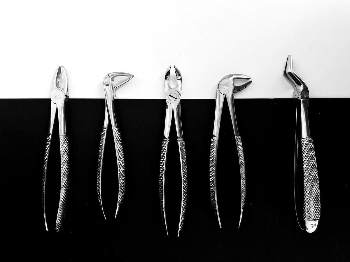 Cinque pinze per estrazioni dentali allineate su fondo bianco e nero